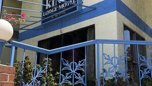 Un motel Kings Lodge con fachada azul y beige, un balcón con barandillas de metal decorativas y plantas en macetas.