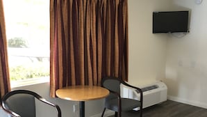 Una habitación con cama, una mesa redonda con dos sillas, un televisor montado en la pared y una ventana con cortinas.