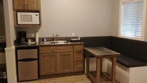 A compact kitchen with a microwave, sink, and a small refrigerator. There's a wooden table and a bench against the wall.