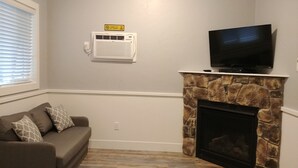 A living room with a stone fireplace, a television mounted above it, and a couch with patterned cushions.