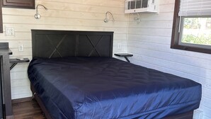A bedroom with a bed, wooden ceiling, built-in air conditioning unit, and a window with blinds.