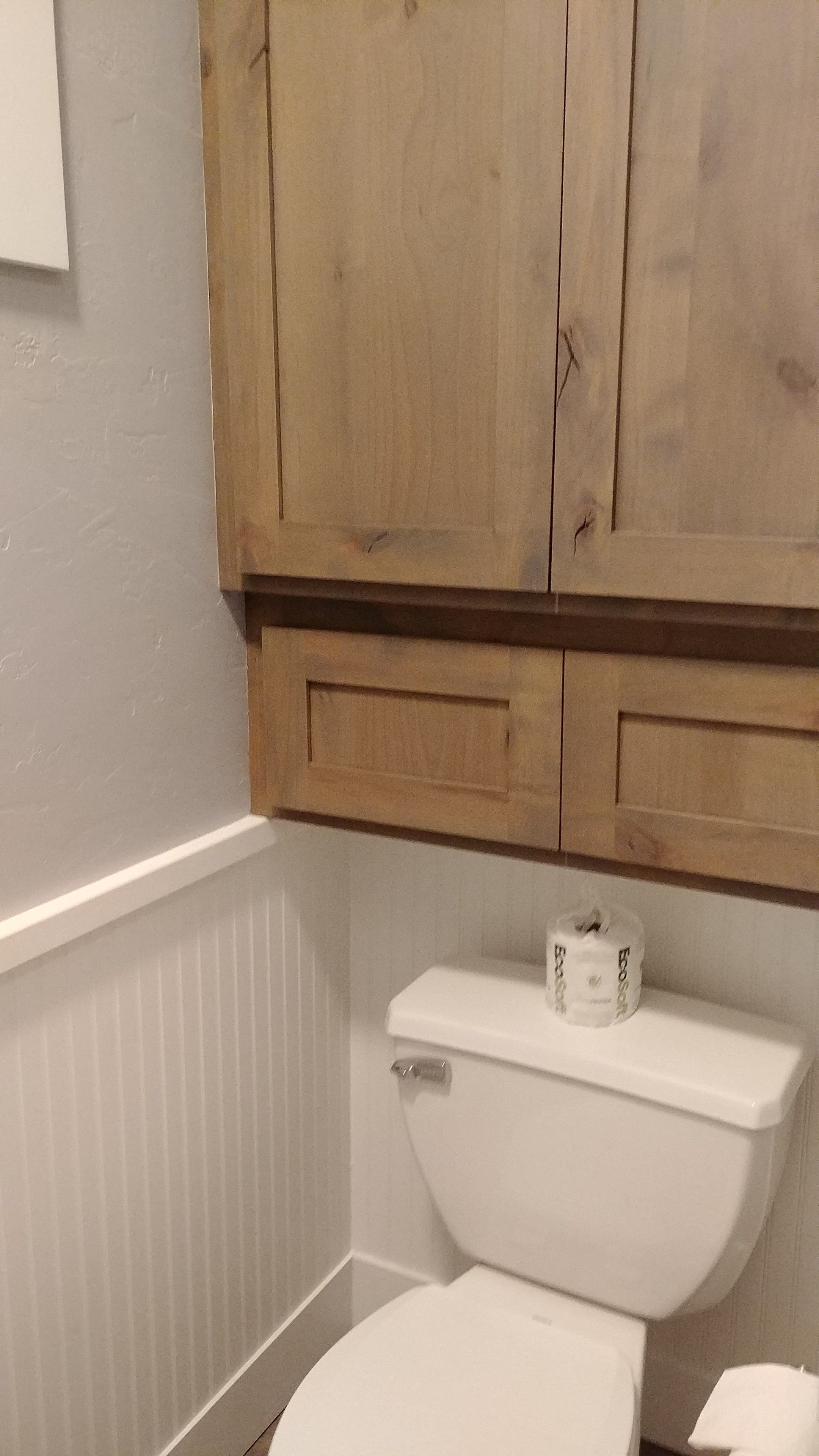 A bathroom with a white toilet, wooden cabinets, and a white baseboard.
