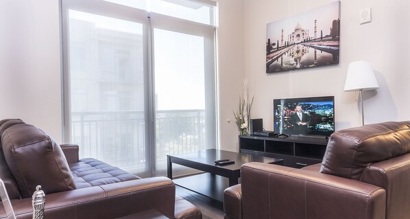 A modern living room with leather sofas, a flat-screen TV, and a large window with a view of the city. - Heaven on Nashville Furnished Apartments (Nashville)