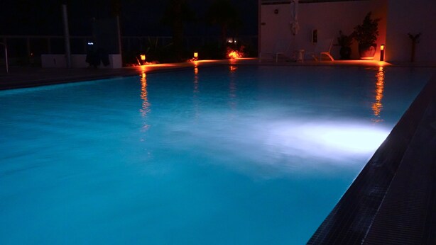 Une piscine dont le bord est recouvert de carreaux et dont l’eau reflète les lumières.