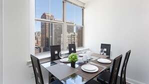 Un coin repas avec une table dressée pour quatre personnes, de grandes fenêtres et une vue sur la ville.