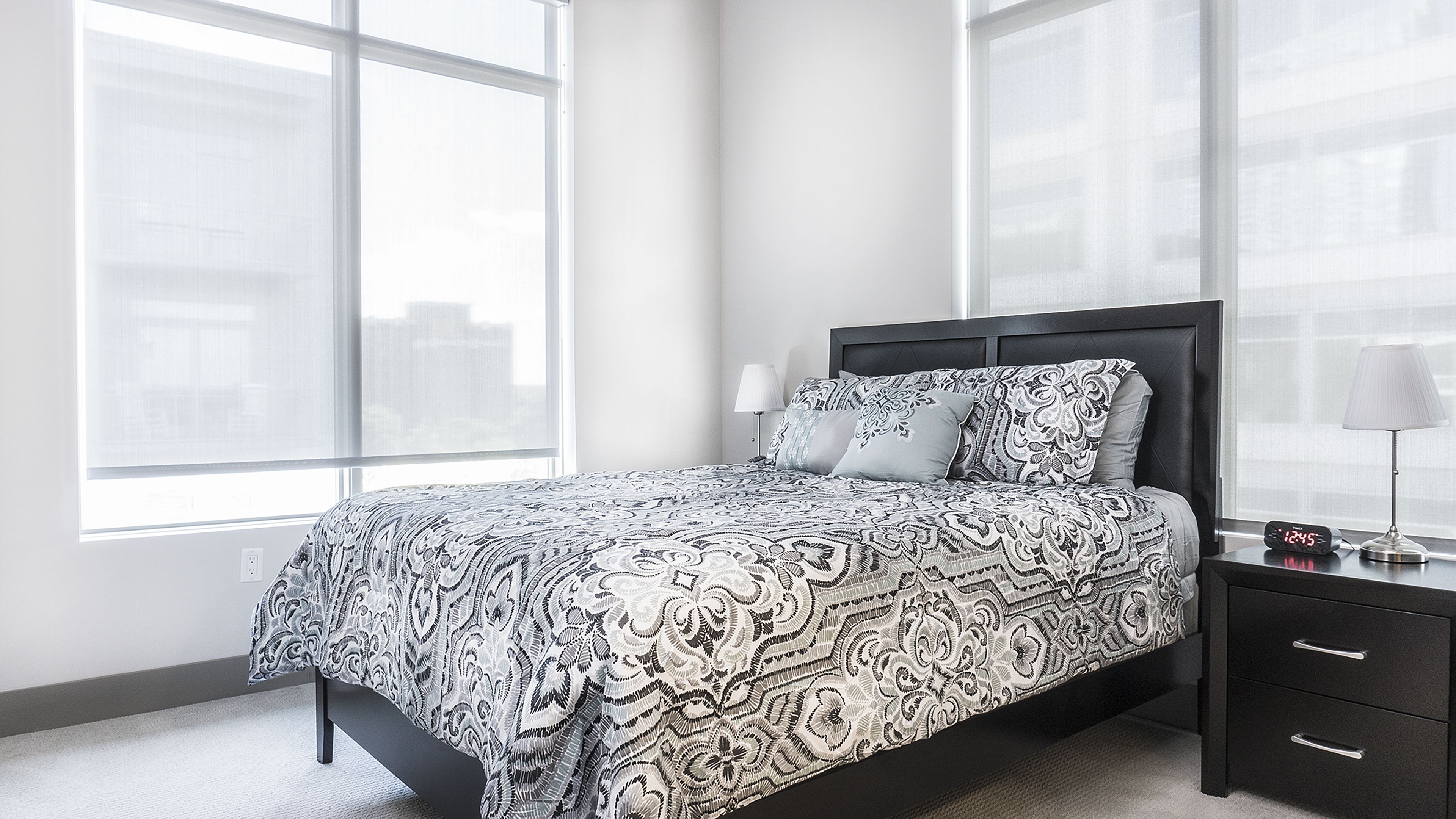 A modern bedroom with a large bed, a nightstand, and a window with blinds.