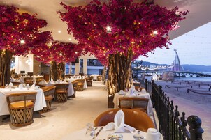 A restaurant with tables set for dining, a view of a bridge, and a beach in the background.