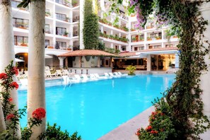 A multi-level hotel with a central swimming pool surrounded by lounge chairs and potted plants. - Playa Los Arcos Resort & Spa All Inclusive (Puerto Vallarta)