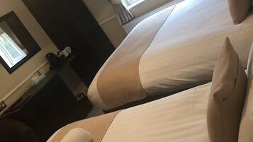 Habitación de hotel con dos camas, un espejo grande, una ventana con cortinas y una mesita con lámpara.