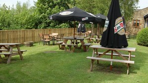 An outdoor patio area with wooden picnic tables and benches, covered by black umbrellas with 'San Miguel' branding. - The Bowes Incline (Chester-le-Street)