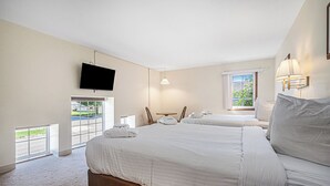 Una habitación de hotel con una cama grande, un televisor montado en la pared, una ventana con vistas al exterior y un balcón.
