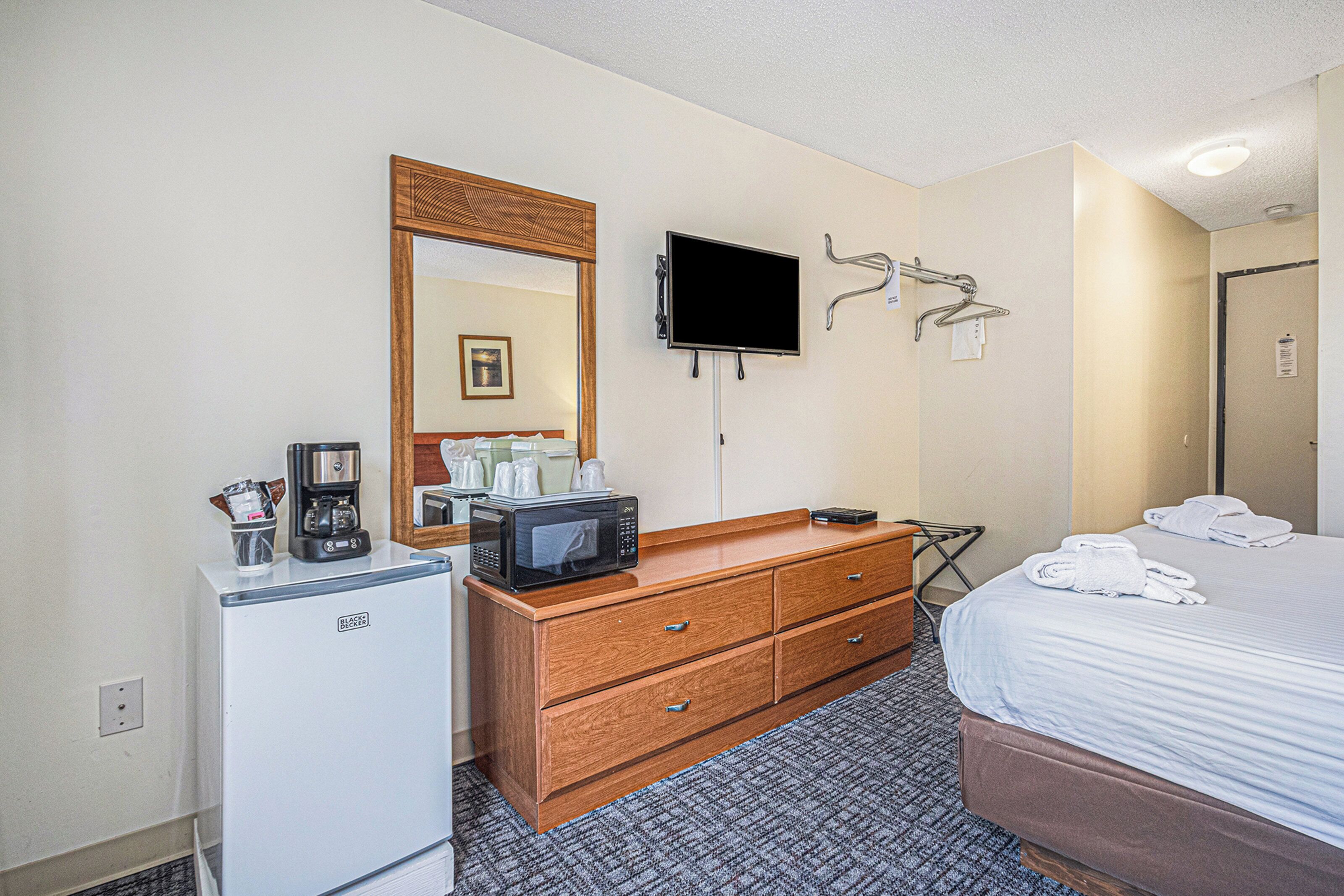 Een hotelkamer met een bed, een dressoir, een magnetron, een koffiezetapparaat, een televisie en een spiegel.