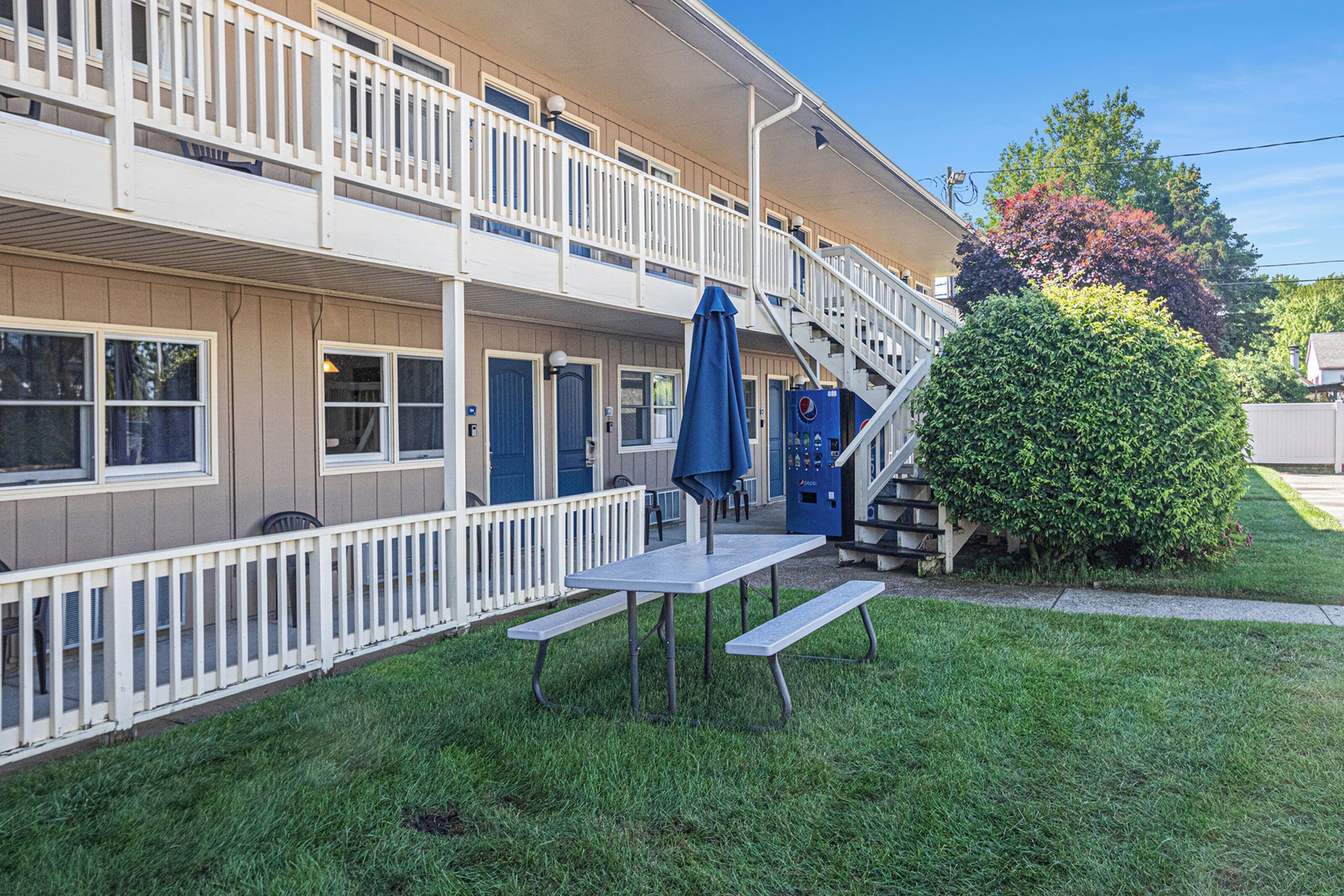 A two-story motel with a covered outdoor seating area and a staircase leading to the upper floor.