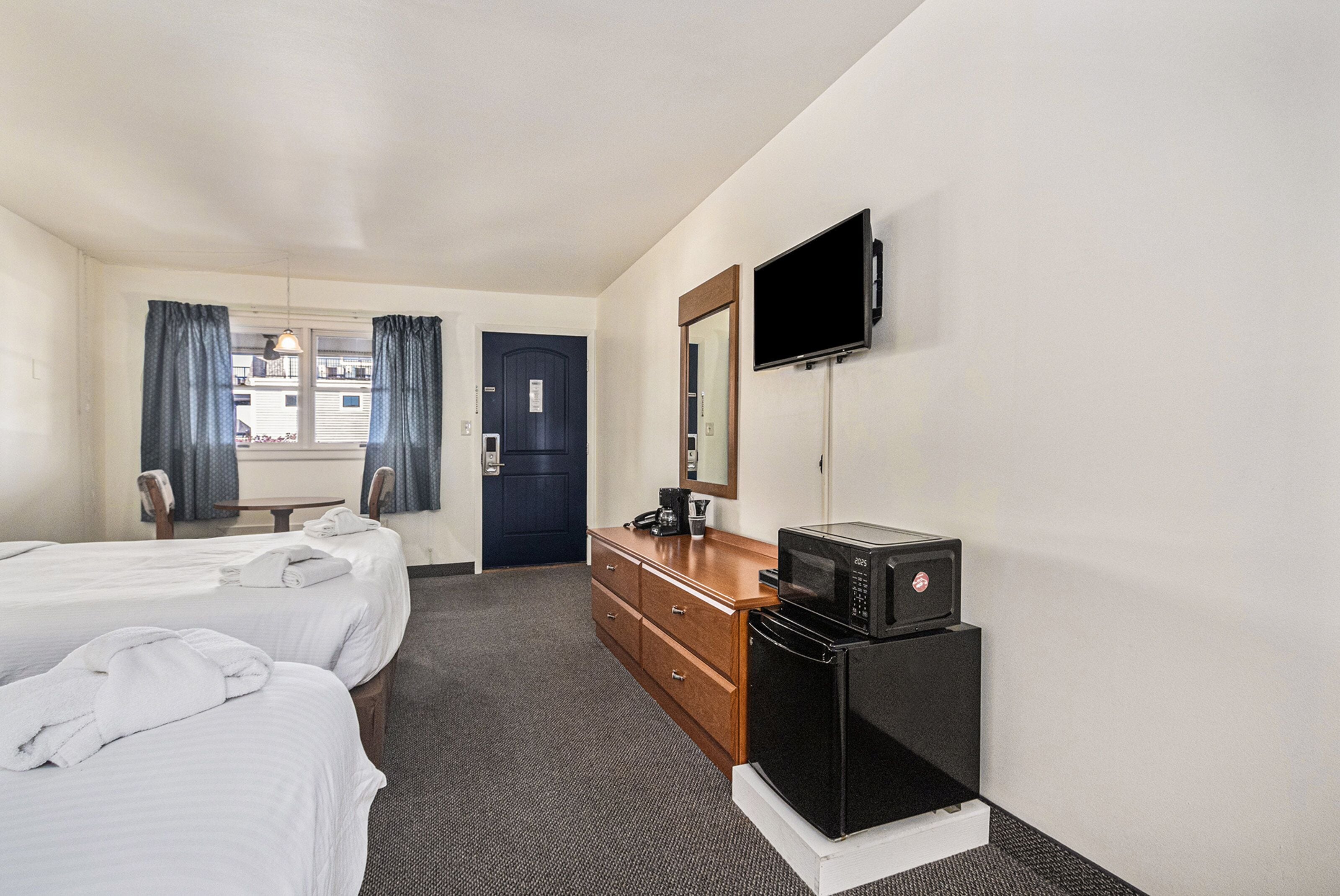 Ein Hotelzimmer mit zwei Betten, einem Schminktisch, einer Mikrowelle, einem Fernseher und einem Fenster mit Vorhängen.