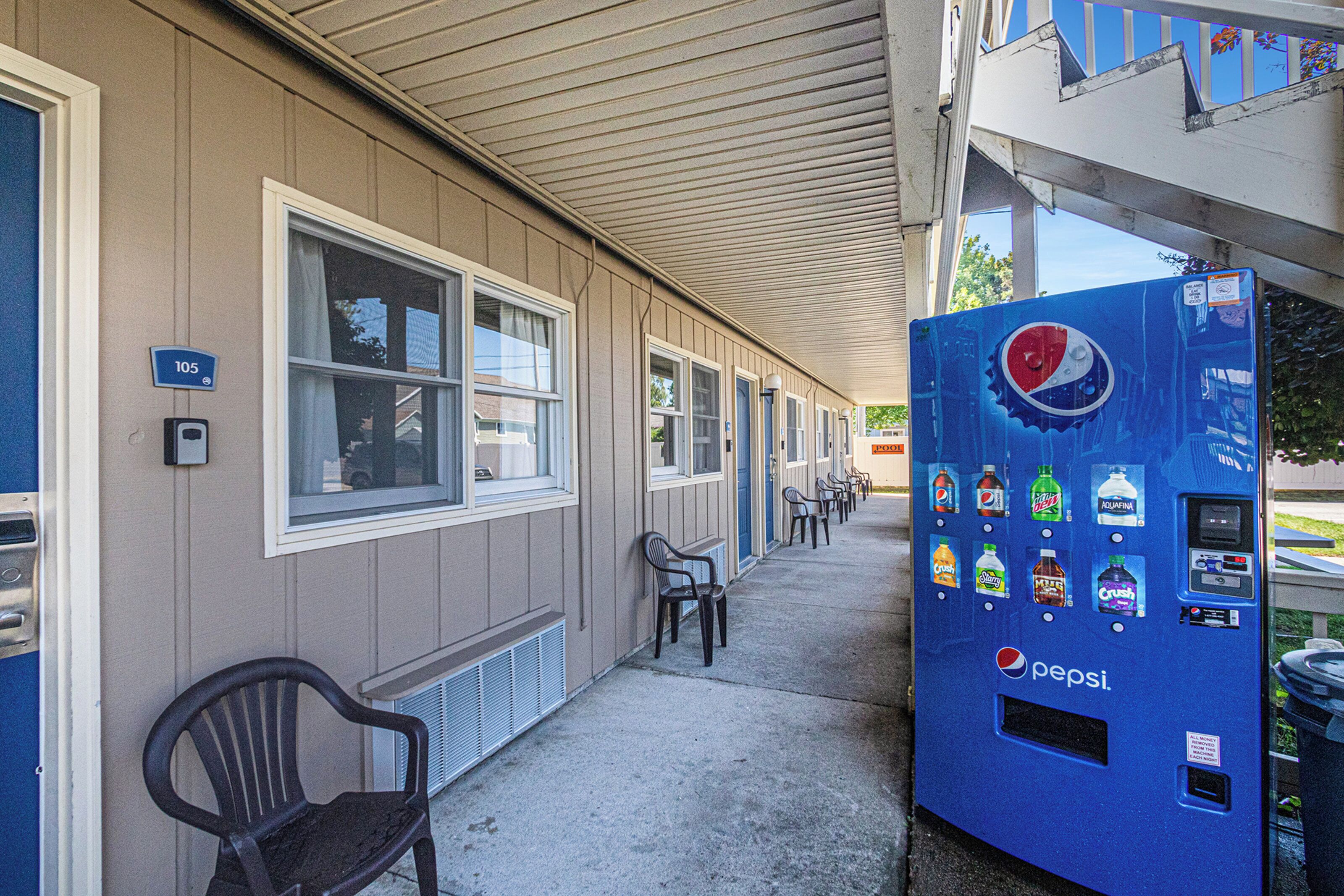 A motel with a row of single rooms, a Pepsi vending machine, and a few plastic chairs outside.