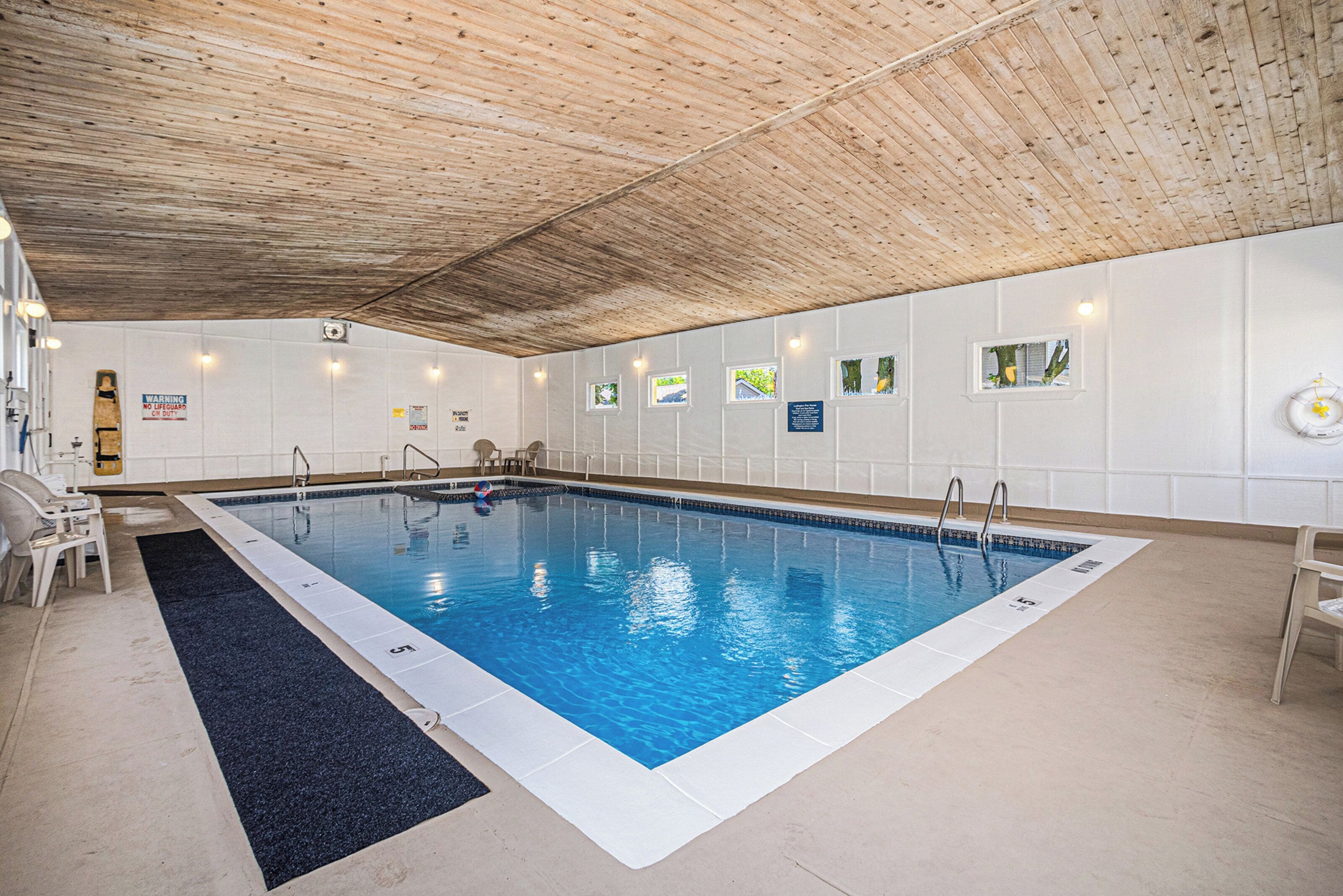 An indoor swimming pool with a wooden ceiling, tiled walls, and a blue pool floor.