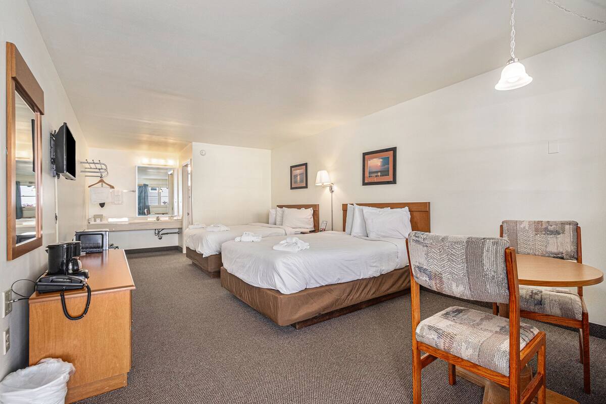 A hotel room with two beds, a desk with a telephone, a chair, a small table, a hanging light fixture, and a mirror.