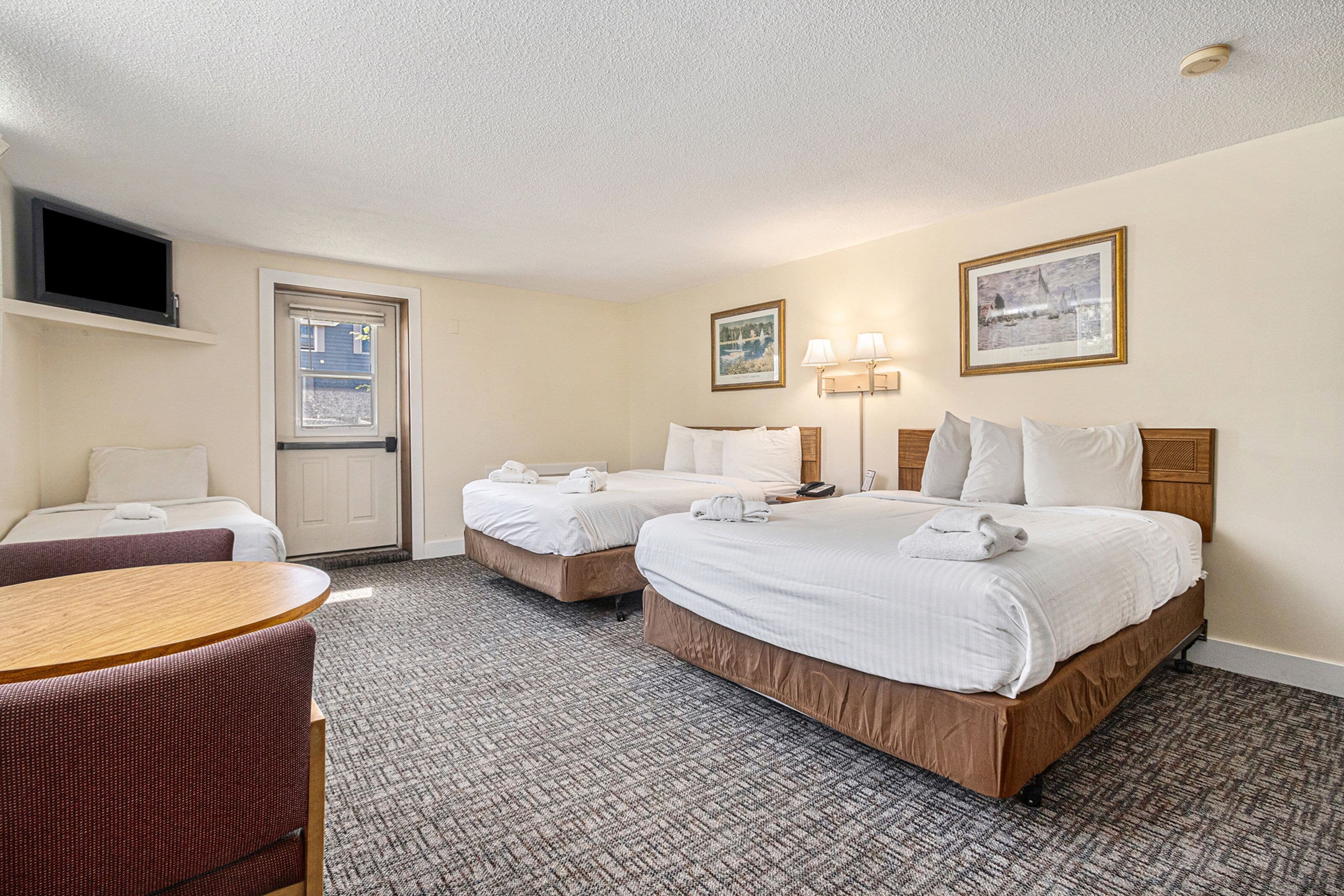 A hotel room with two beds, a desk, a chair, a television, and two framed pictures on the wall.