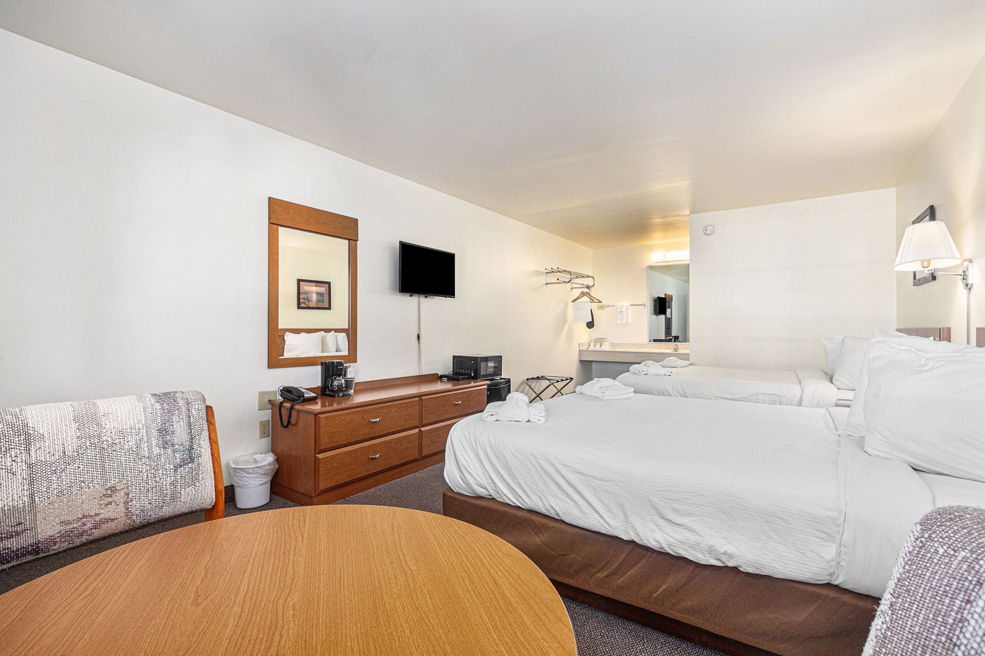 A hotel room with a bed, a desk, a chair, a dresser, a TV, and a mirror.