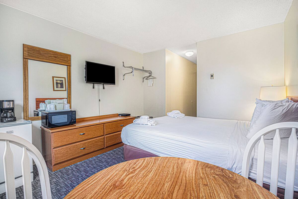 A hotel room with a bed, a desk with a microwave, a television, and a chair.