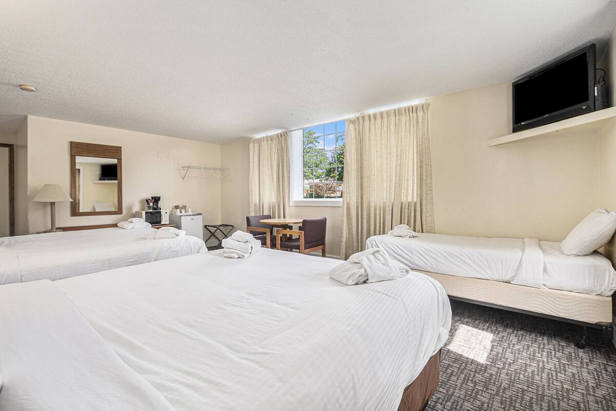 A hotel room with two beds, a desk, a chair, a TV, and a window with curtains.
