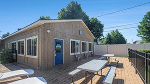 Un edificio de madera con puerta azul, ventanas grandes y mesas de picnic en una terraza de madera.