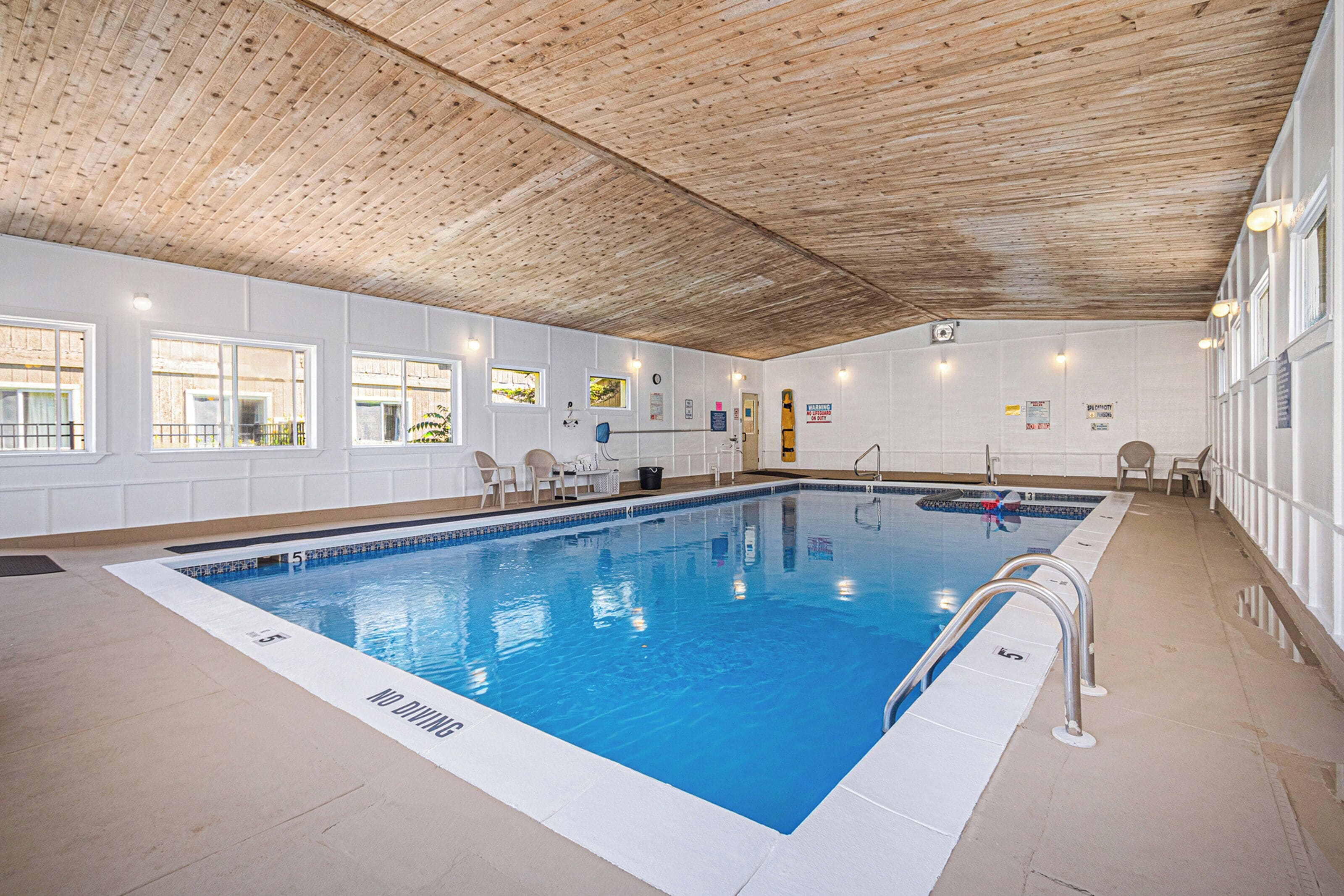 Una piscina interior con techo de madera, paredes blancas y suelo de baldosas.