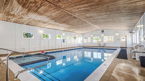 Una piscina interior con techo de madera, paredes blancas y ventanas pequeñas.