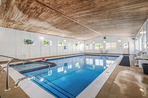 An indoor swimming pool with a wooden ceiling, white walls, and small windows. - Ludington Pier House (Ludington)