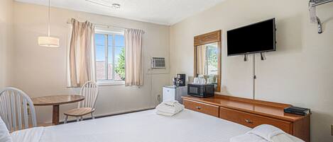 Habitación de hotel con cama, escritorio, silla, televisor, microondas y ventana con cortinas.