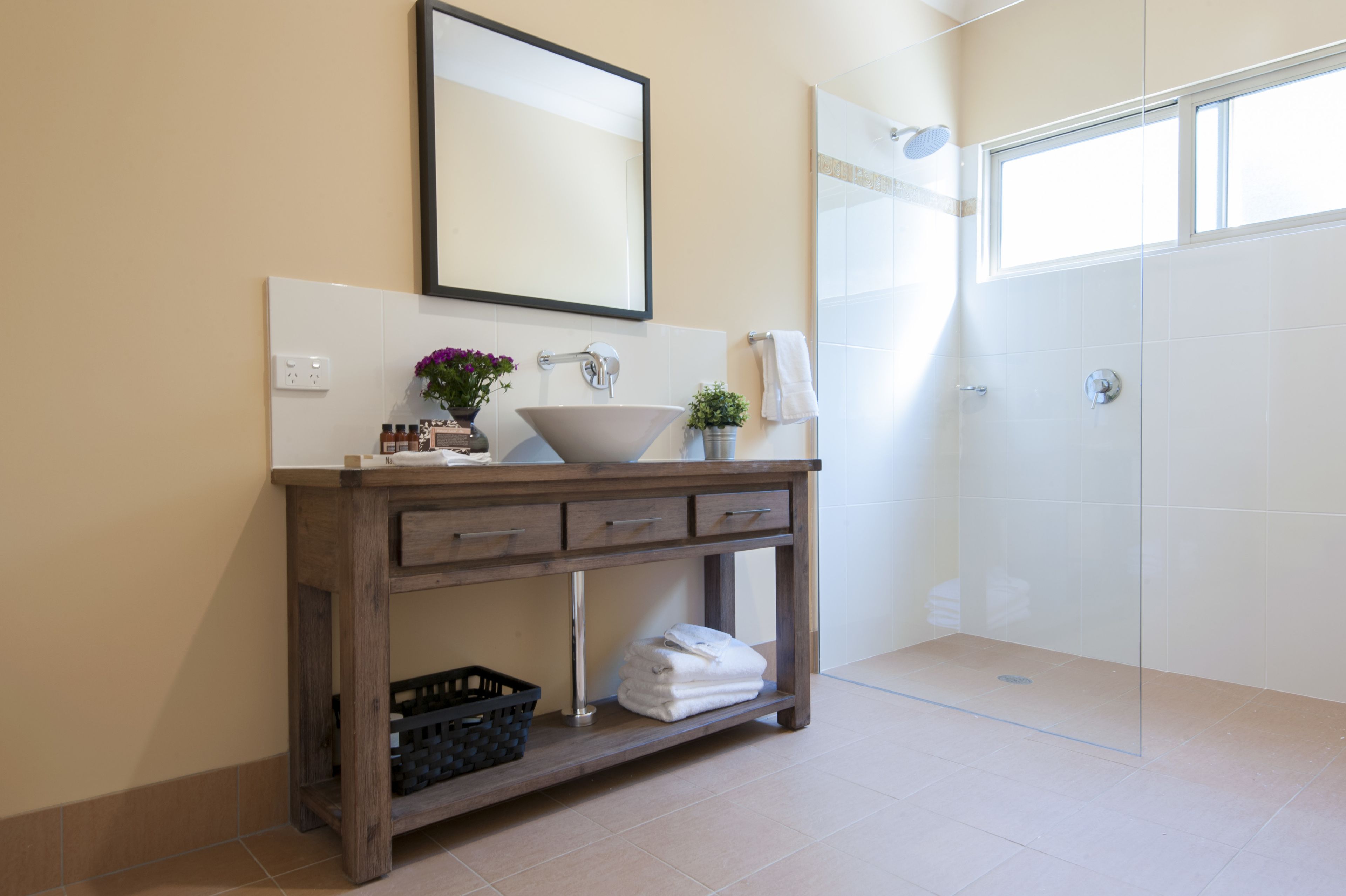 A bathroom with a wooden vanity, a large mirror, a sink, and a shower area.