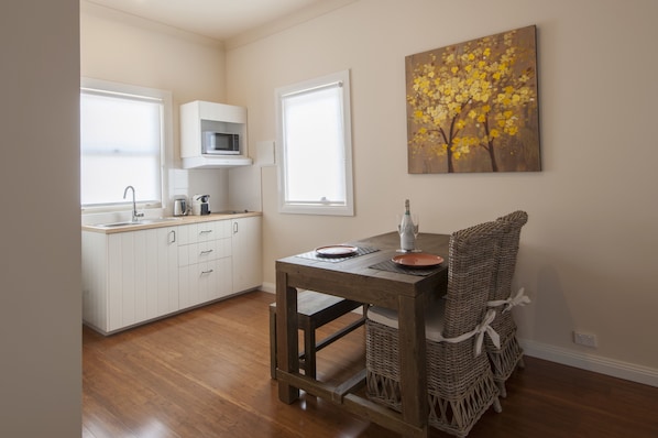 A kitchen with white cabinets, a microwave, and a dining table with wicker chairs. - The Nest at Gundaroo (Gundaroo)