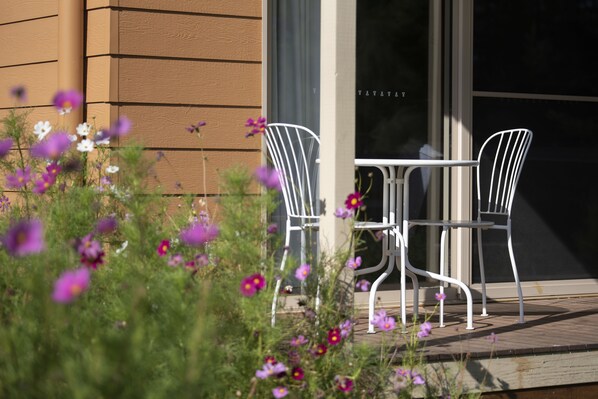 An outdoor seating area with metal chairs and a table, surrounded by flowering plants.