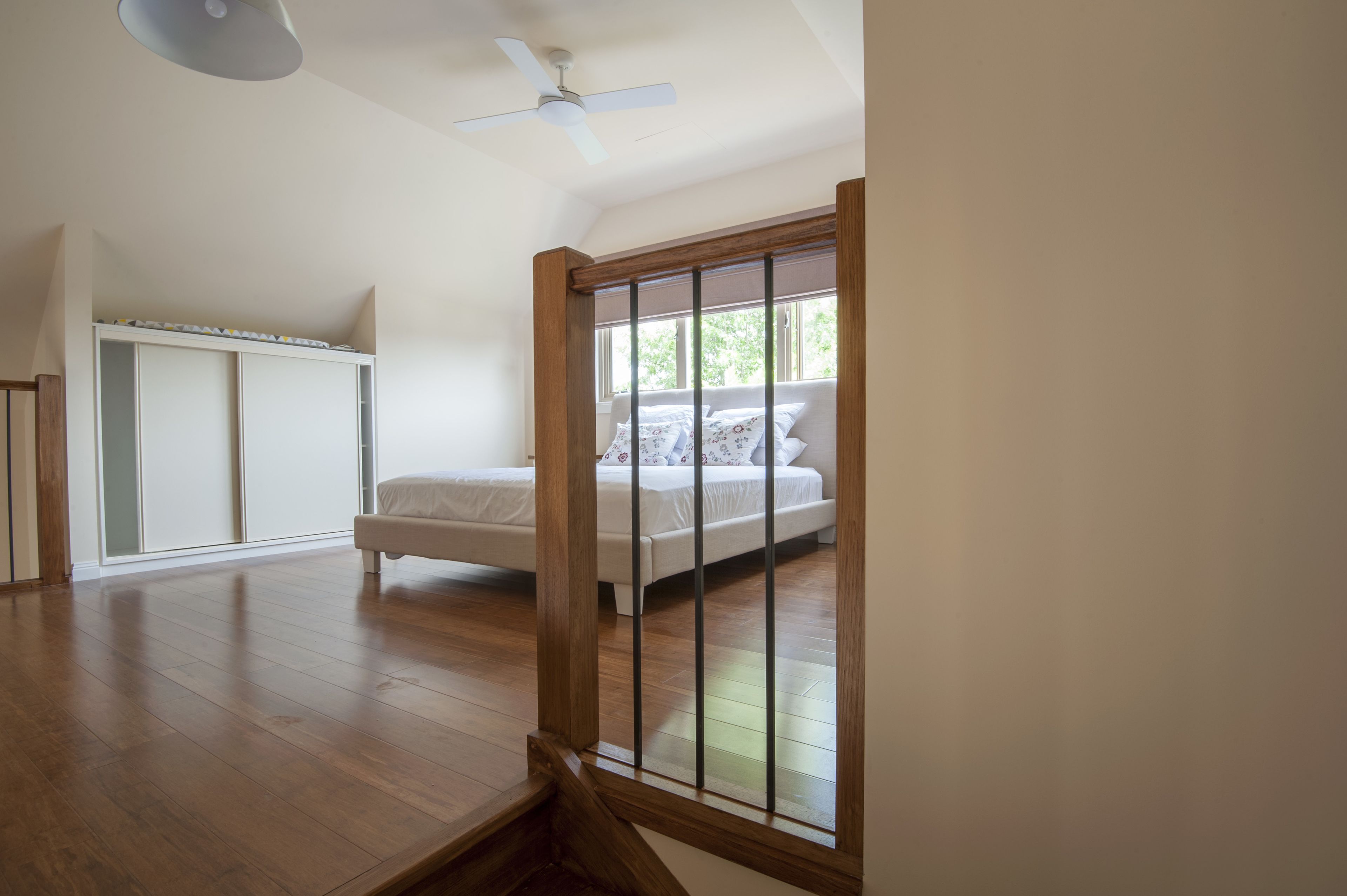 A bedroom with a bed, a ceiling fan, and a window with a view of greenery.