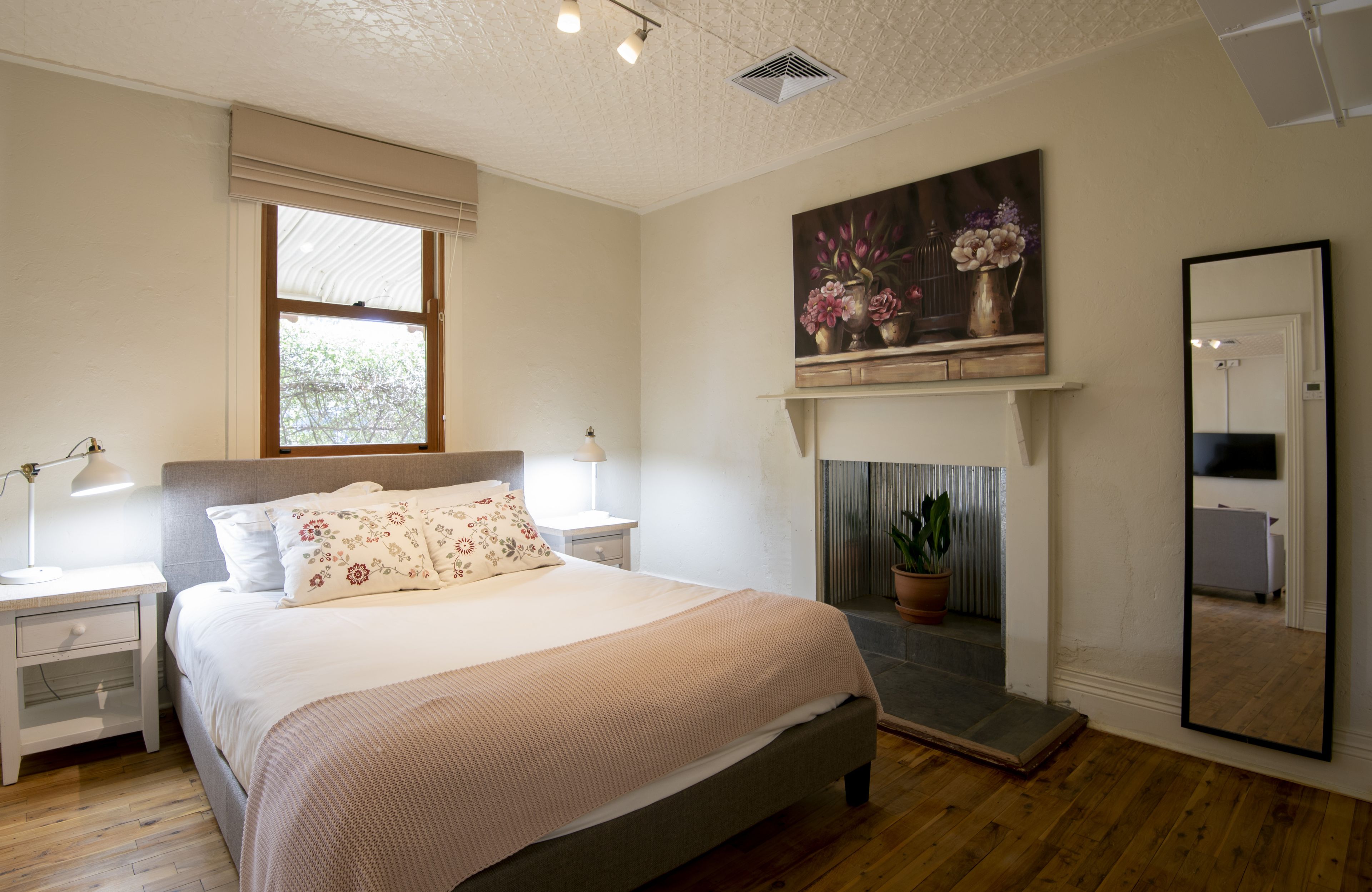 A bedroom with a bed, bedside tables, a mirror, a fireplace, and a window.