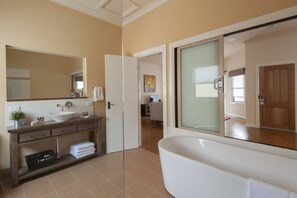 Un baño moderno con una bañera grande, un tocador con lavamanos y espejo, y una puerta que conduce a otra habitación.