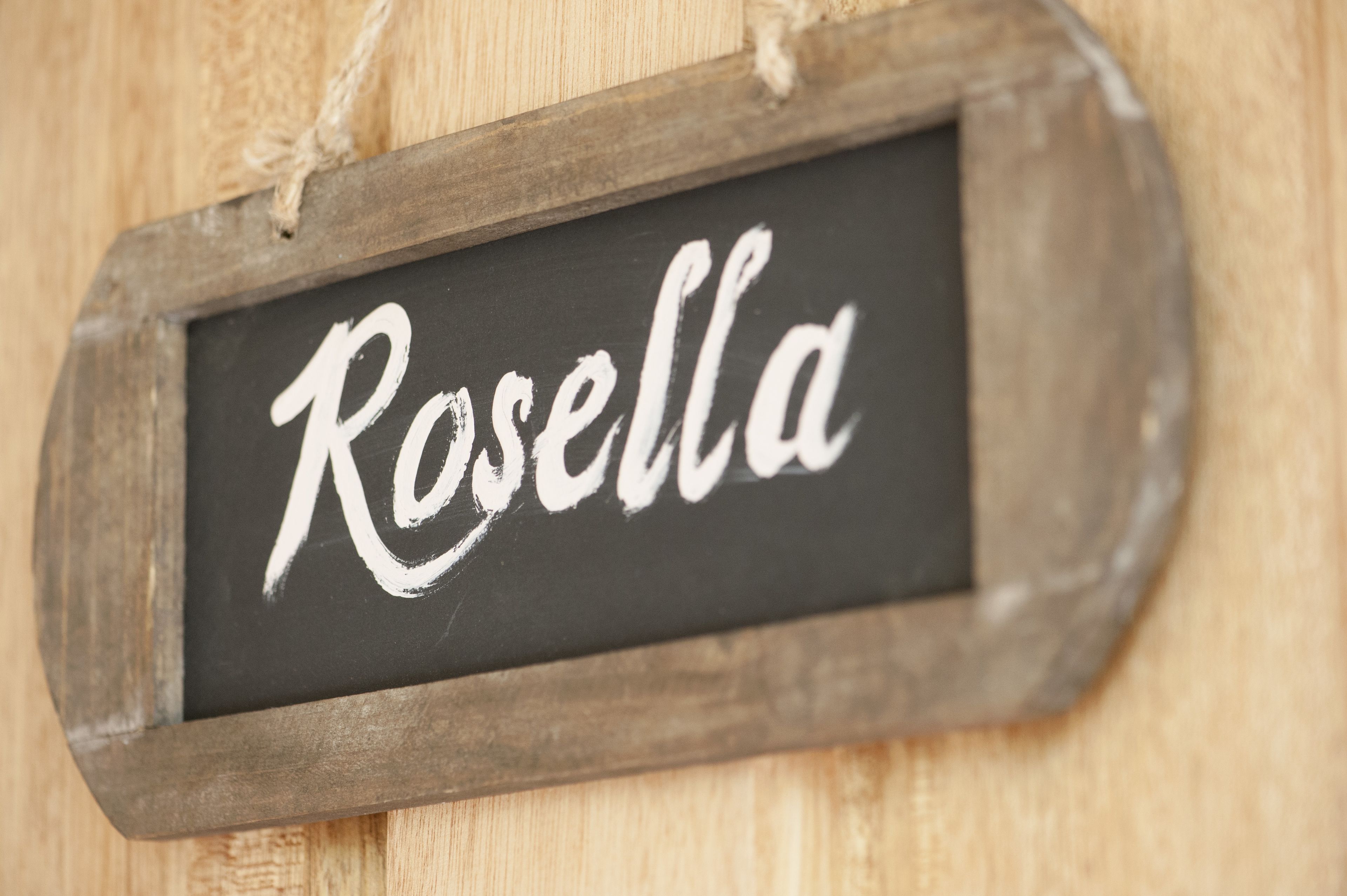 A rustic wooden sign with the name "Rosella" written in white chalk on a black background.