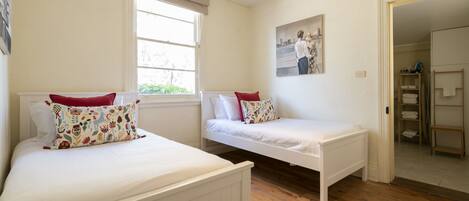 Un dormitorio con dos camas individuales, una ventana, un cuadro y suelo de madera.