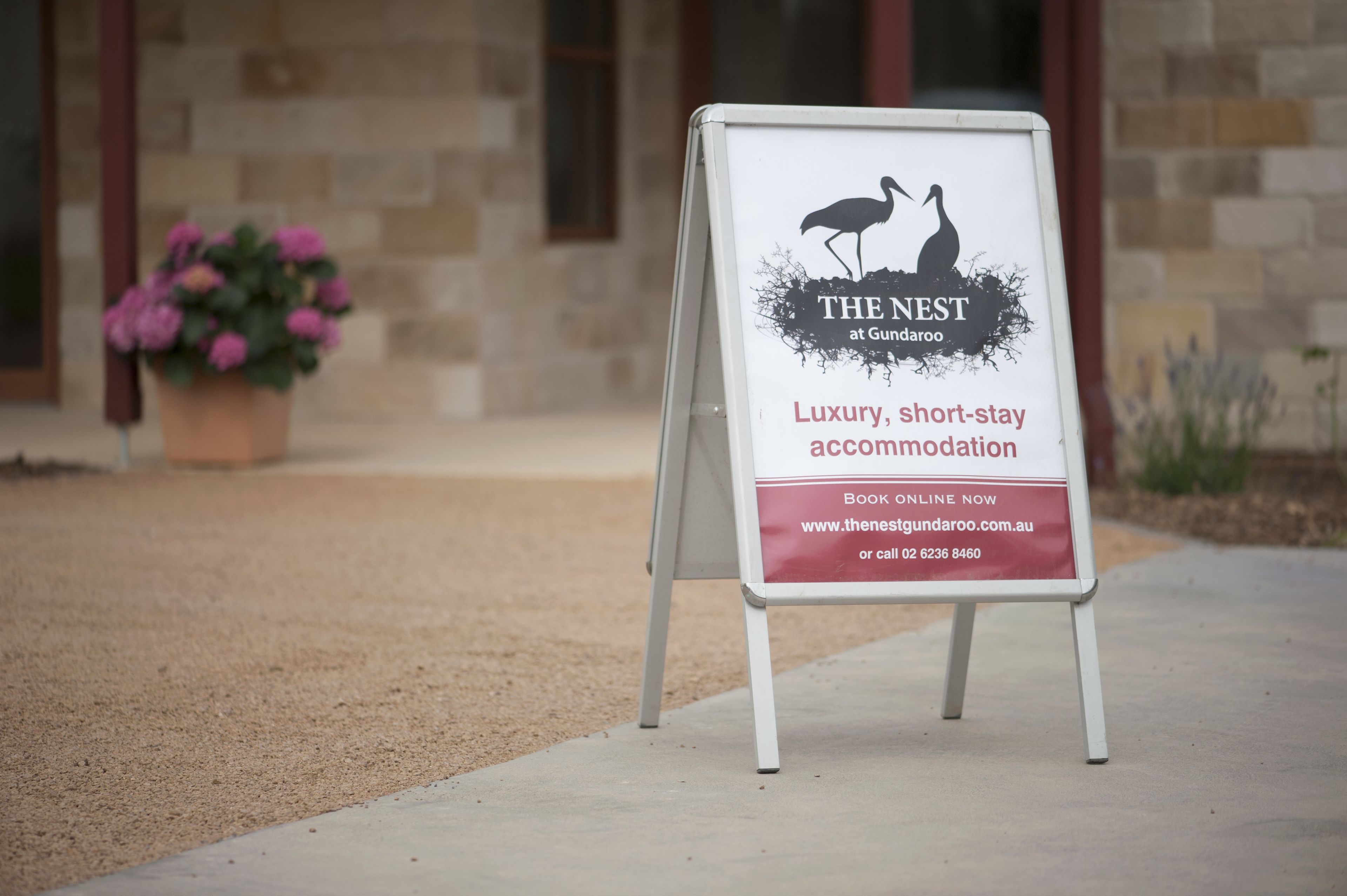 A signboard for "The Nest at Gundaroo" advertising luxury, short-stay accommodation with an online booking option and a phone number.