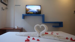 A hotel room with a bed, a TV on a blue shelf, and a heart-shaped towel decoration. - Den'gi Inn (El Nido)