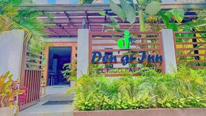 A building with a sign reading "Den'gi Juma" and a large palm tree in front. - Den'gi Inn (El Nido)