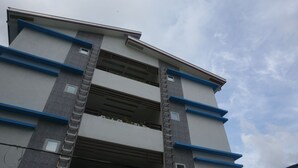 A multi-story building with a curved roofline, a central staircase, and a series of windows on each floor. - Den'gi Inn (El Nido)