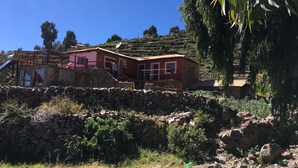 A rustic stone house with a red roof, a small balcony, and a solar water heater. - Muña Wasi & Lodge (Isla Amantani)