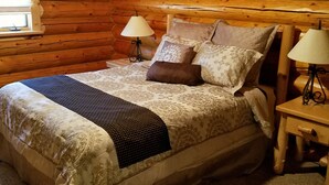 Ein Schlafzimmer in einer Blockhütte mit einem Bett, zwei Nachttischen mit Lampen und einem Fenster.