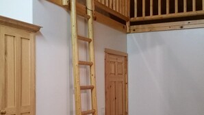 Ein Zimmer mit einer Holzleiter, die zu einem Schlafbereich im Zwischengeschoss führt, Holztüren und einer geneigten Decke.