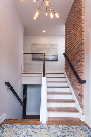 Staircase with a modern design, featuring white steps and wooden accents, flanked by a brick and white wall.