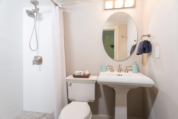 Un baño con ducha, inodoro, lavabo y espejo.