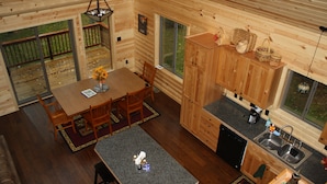 Interior de una cabaña de madera con comedor, cocina y ventanas amplias.