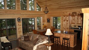 Un interior de cabaña espacioso con comedor de madera, una sala de estar acogedora con sofá y una mesa de centro, y una cocina con barra.