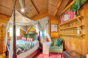 A wooden room with a canopy bed, a green armchair, and a shelf with decorative items.